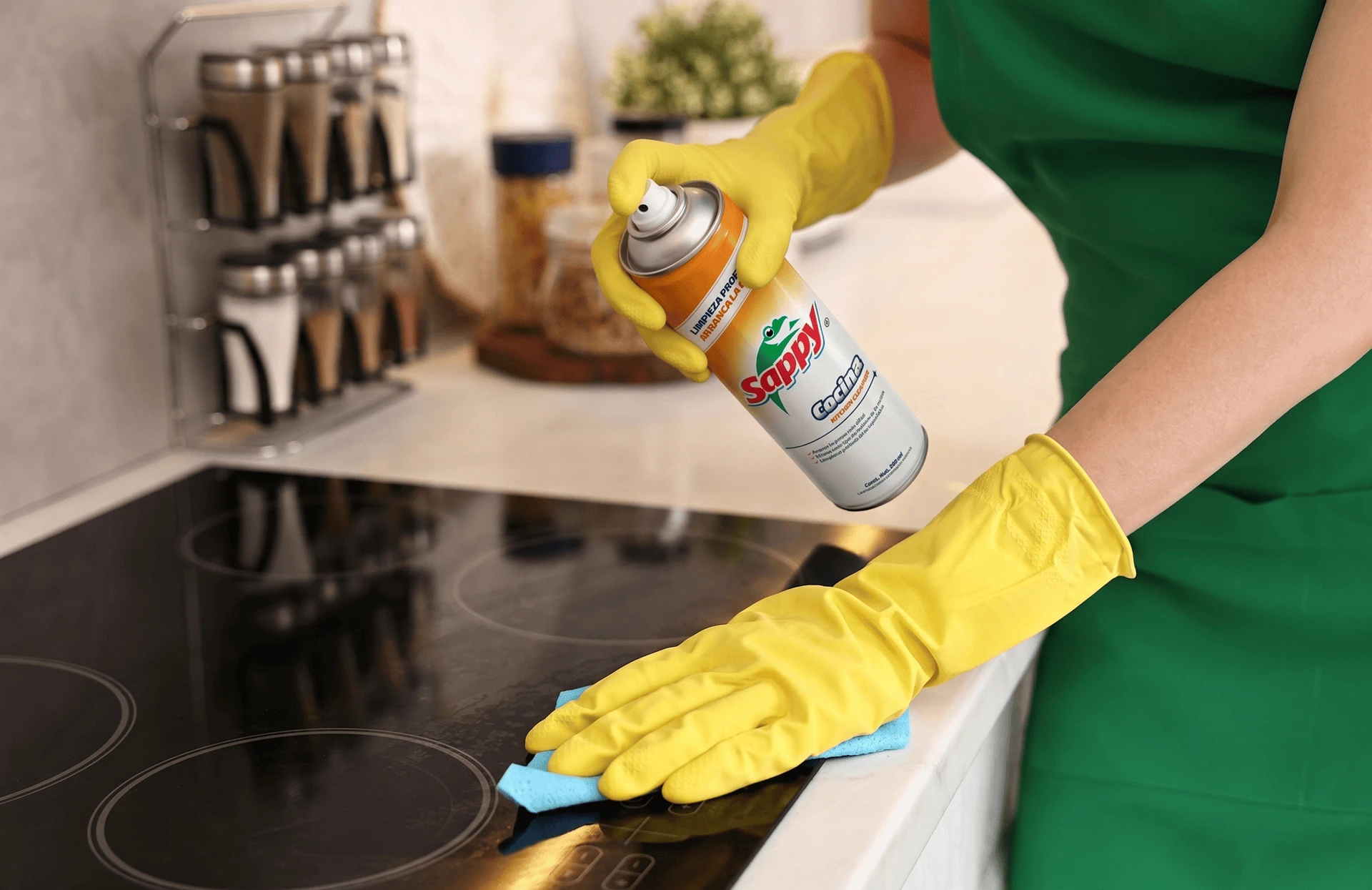 Mujer con guantes amarillos y producto Sappy en la mano limpiando una tarja de cocina.